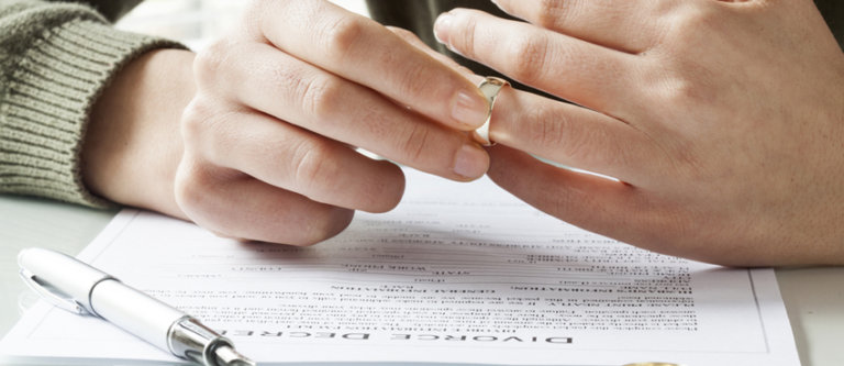 Person taking off wedding ring over divorce papers