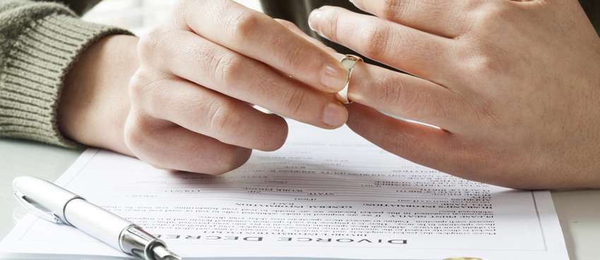 Person removing wedding ring as they're looking at divorce papers